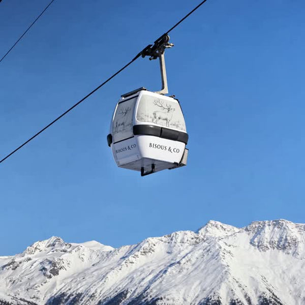 Bisous & Co ski gondola above snowy mountains under a clear blue sky