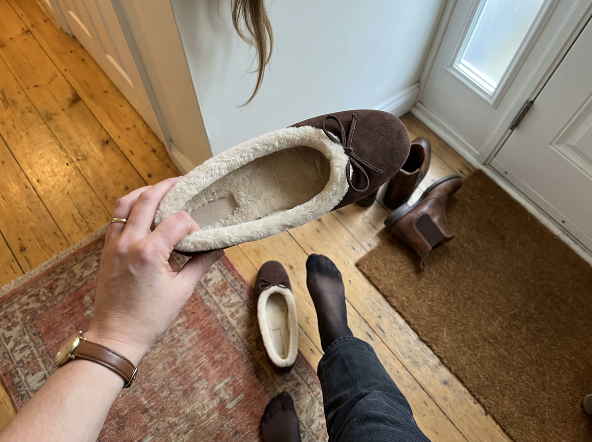 A hand holds the Courchevel Flat in Chocolate open at the front door, showing the cream plush inside and the plush rim all around