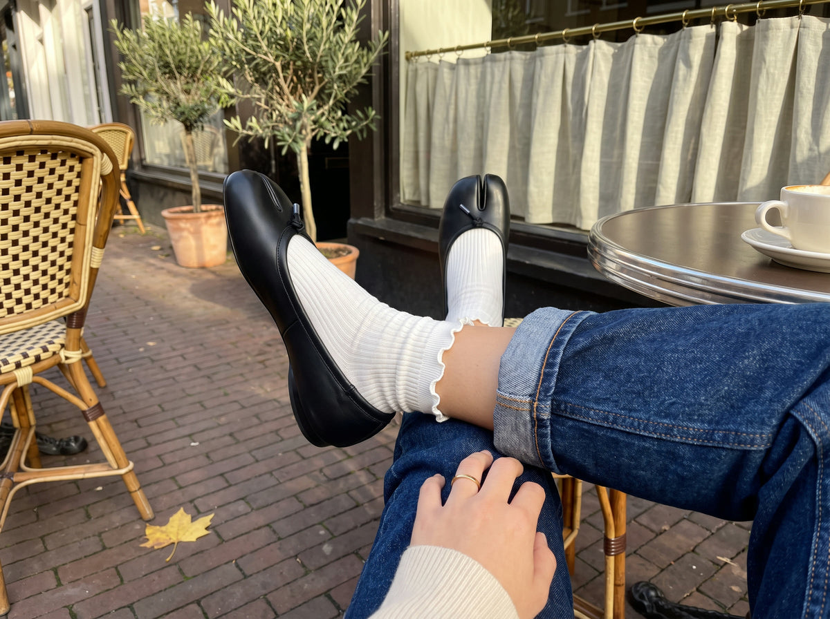 Black split-toe ballet flats with white ruffle socks under rolled straight jeans at a café table