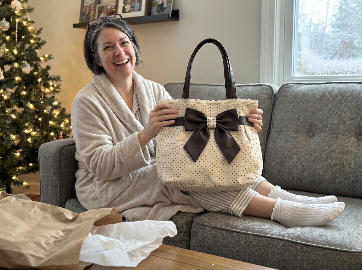 A woman laughs on her sofa on Christmas morning holding the Paris Bow Tote in Cream, white ruffle socks on her feet
