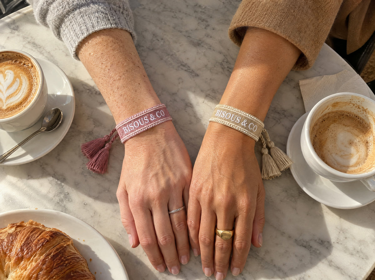 Two friends at a cafe table with their wrists side by side, one in Dusty Rose and one in Sand