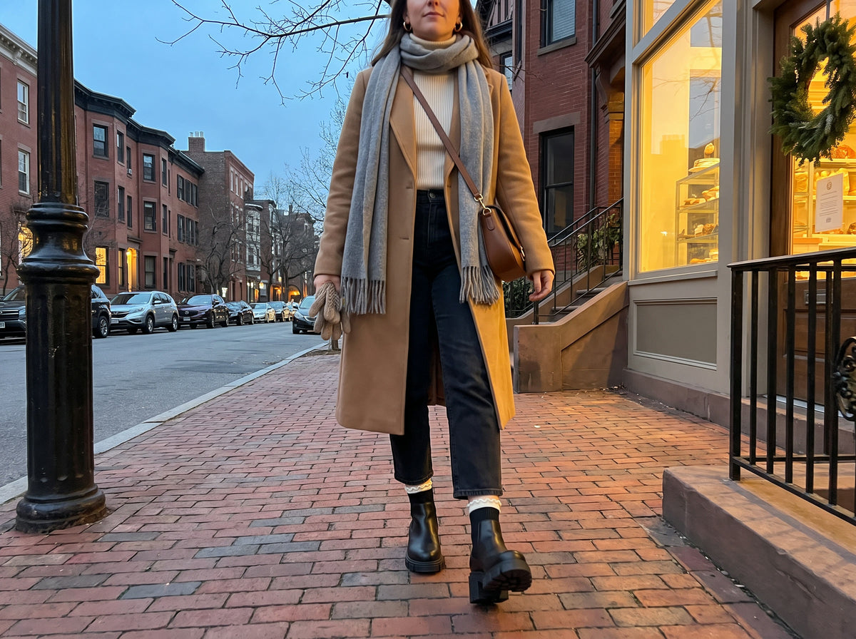 A woman walks a brick sidewalk at dusk in January in the Vienna Boot in Black, white ruffle socks folded over the knit collar